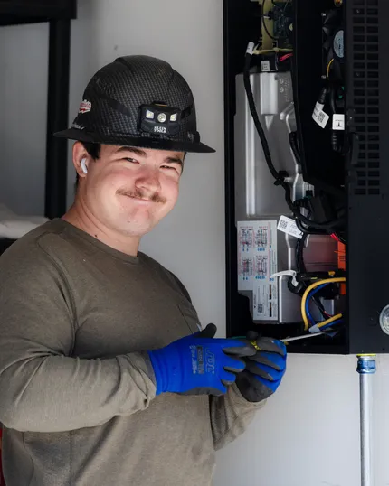 Worker in hard hat and blue gloves using a tool inside an open computer server cabinet.