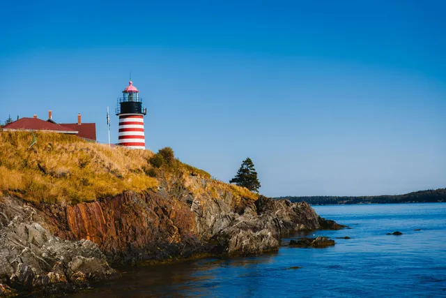 Red-and-white lighthouse on rocky coastline above blue water under a clear sky