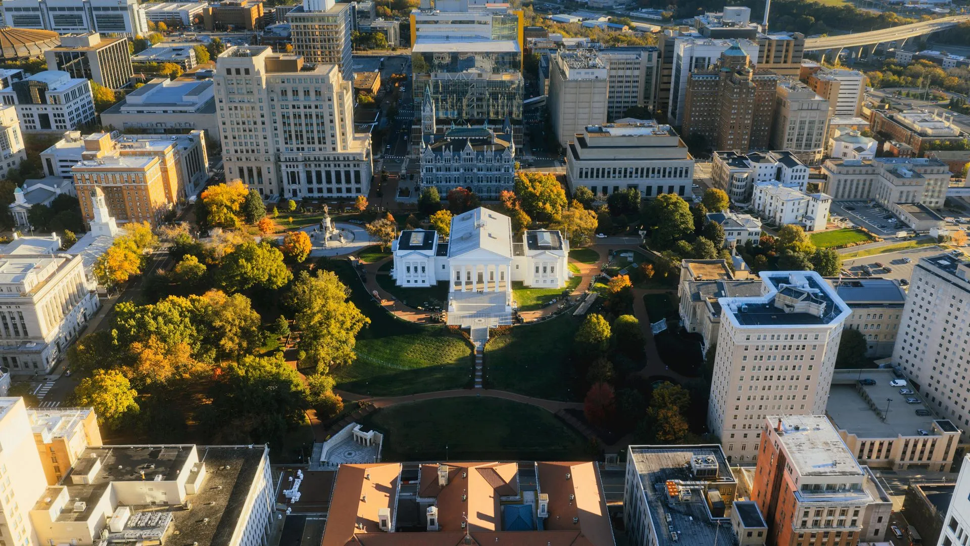 Aerial view of a city center with a white building, park, and surrounding tall buildings at sunset