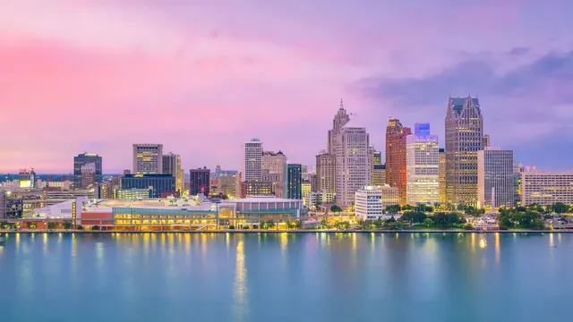 Colorful city skyline at sunset reflected on calm water under a pink sky