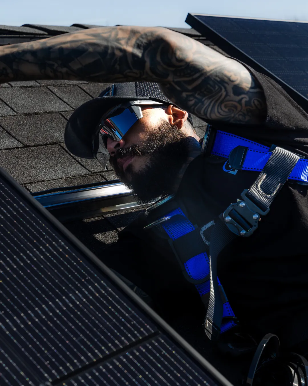 An aerial view of a house with solar panels on the roof Worker in blue harness emerging through a roof hatch, shading his eyes in bright sunlight.