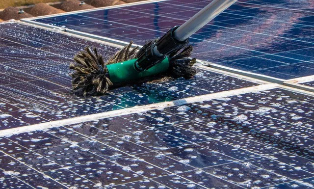 A person is cleaning a solar panel with a brush.