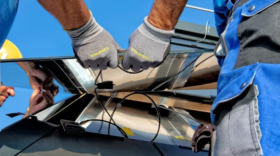 Gloved hands working on cracked black glass or windshield outdoors under a blue sky.