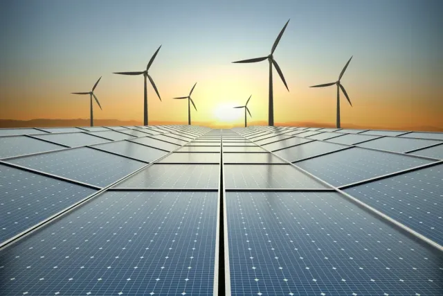 A field of solar panels and wind turbines at sunset.